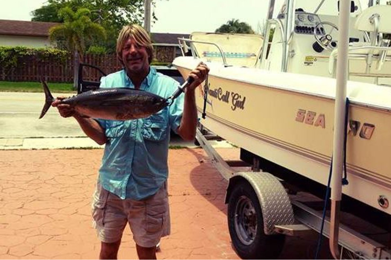 Captain Kevin holding a freshly caught tuna next to NautiCall Girl